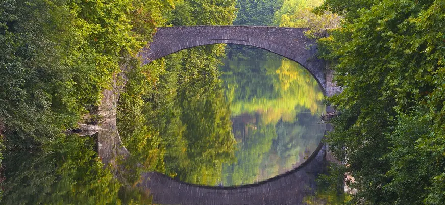 Puente de piedra reflejado en el río rodeado de vegetación en Bera, creando un arco perfecto.