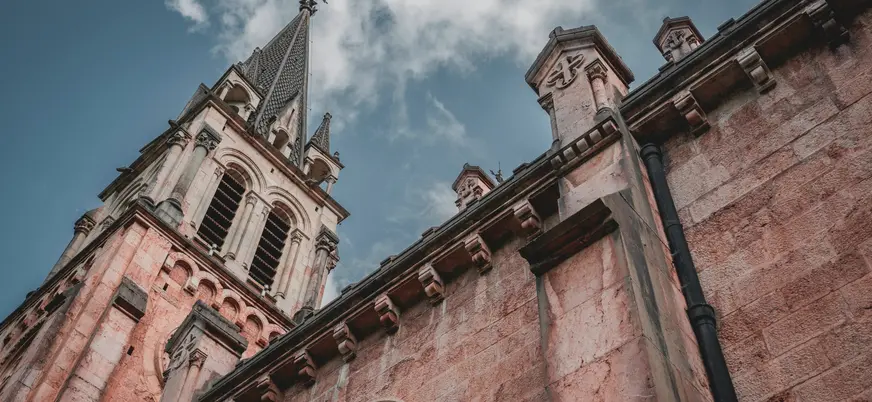 Detalle arquitectónico del Santuario de Covadonga en Asturias, con su torre neogótica destacando bajo un cielo azul con nubes.