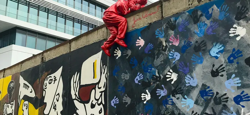 Escultura roja sobre el Muro de Berlín con murales y huellas de manos en el East Side Gallery