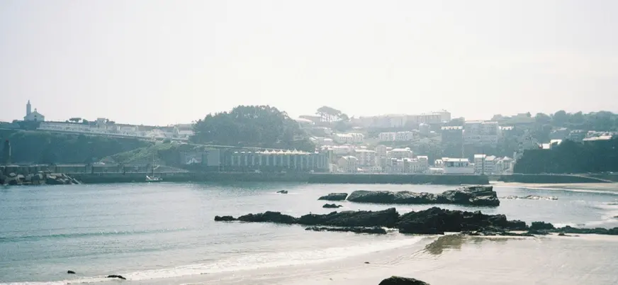 Playa de Luarca, Asturias, con rocas oscuras, arena y el pueblo costero en el horizonte.