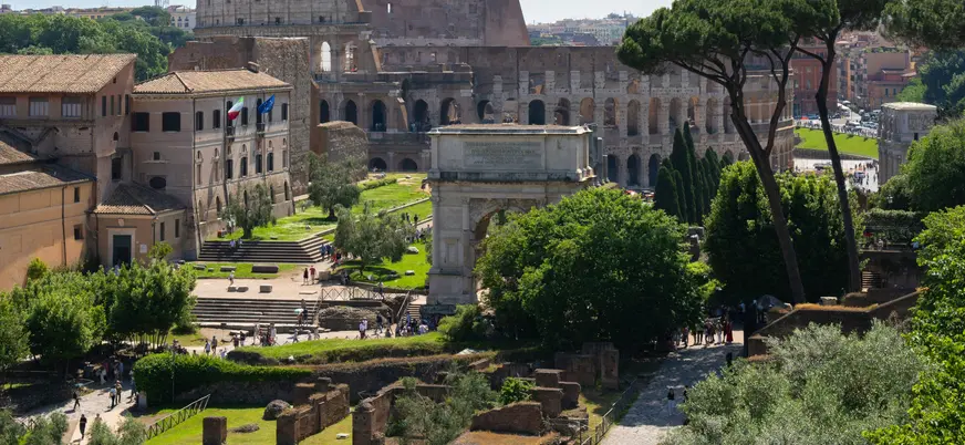 Vista del Coliseo y el Arco de Constantino desde el Foro Romano, rodeados de vegetación.