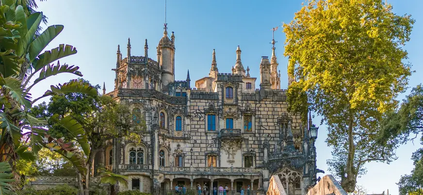 Fachada del palacio de la Quinta da Regaleira rodeada de árboles en un día soleado.