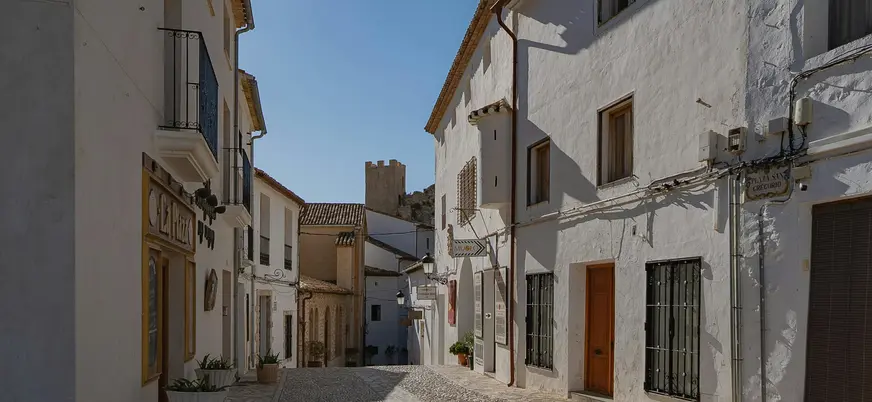 Calle empedrada con casas blancas en Guadalest, con la torre del castillo al fondo.