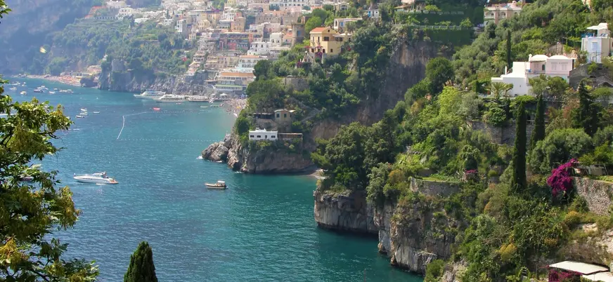 Vista de la Costa Amalfitana, con casas enclavadas en los acantilados y pequeñas embarcaciones en el mar. 