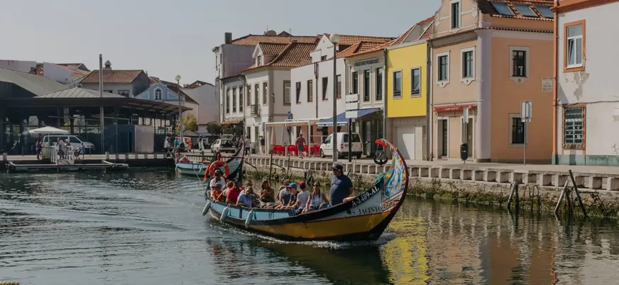 Moliceiro con turistas navegando por un canal de Aveiro junto a casas coloridas.