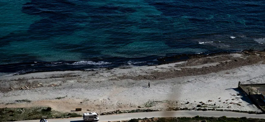 Vista aérea de una playa de arena y rocas con caravanas y una persona, junto al mar turquesa de Santa Pola.