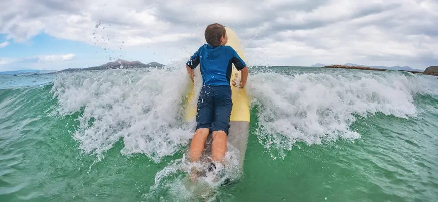 Niño sobre tabla de surf cruzando una ola en Mundaka, Vizcaya
