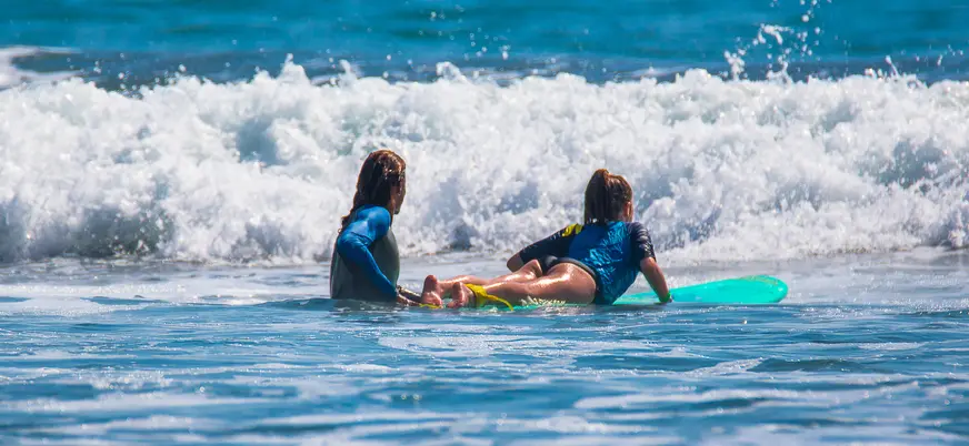 Profesor ayudando a una niña sobre su tabla de surf en el mar de Mundaka, Vizcaya
