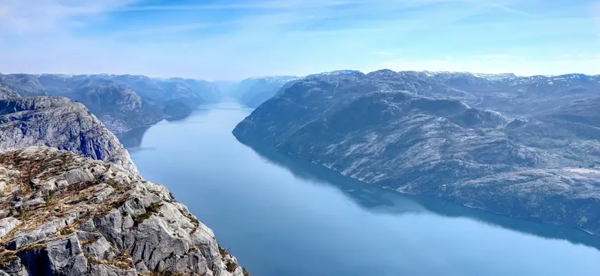 Vista panorámica del fiordo Lysefjord en Noruega, con acantilados rocosos y aguas tranquilas bajo cielo despejado.
