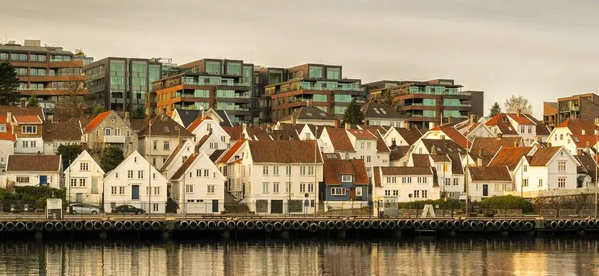 Casas tradicionales de madera en Stavanger, Noruega, frente al puerto con reflejos dorados al atardecer.