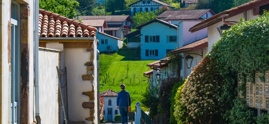 Persona caminando entre casas blancas y verdes prados en Ainhoa, en el País Vasco francés.