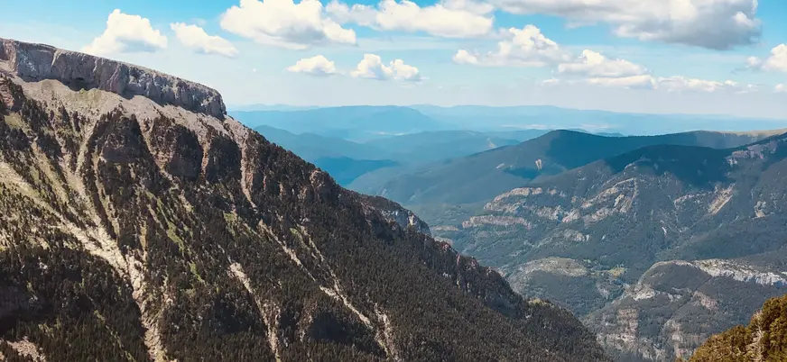 Vistas panorámicas del Valle de Canfranc, Pirineo Aragonés, con laderas boscosas y picos bajo un cielo azul con nubes.
