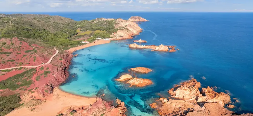 Vista aérea de Cala Pregonda con sus aguas turquesas y rocas rojas en Menorca