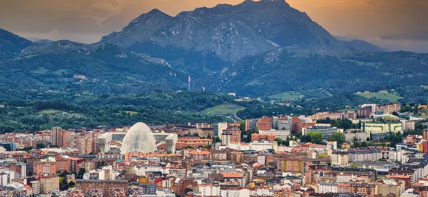 Vista panorámica de Oviedo con el Palacio de Exposiciones y Congresos y las montañas asturianas al fondo al atardecer.