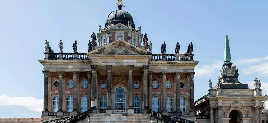 Fachada y escalinata principal del Nuevo Palacio (Neues Palais) en Potsdam, con estatuas y cúpula barroca.