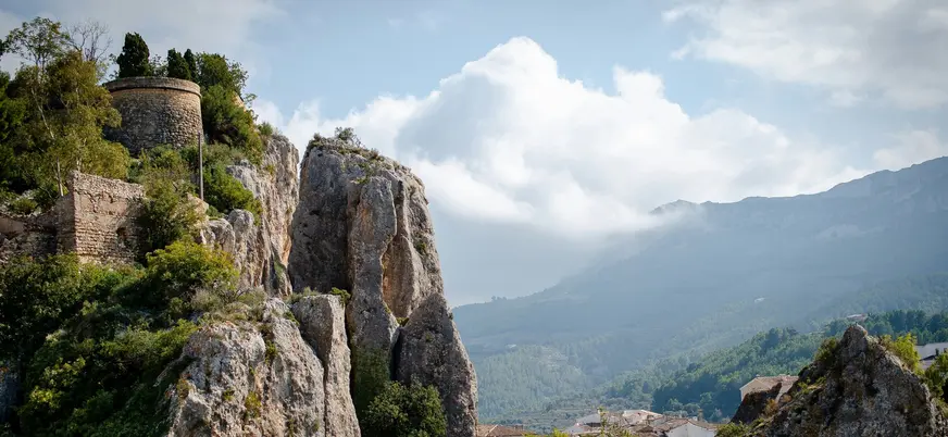 Vista del castillo de Guadalest sobre rocas y montañas, con el valle y el pueblo al fondo.