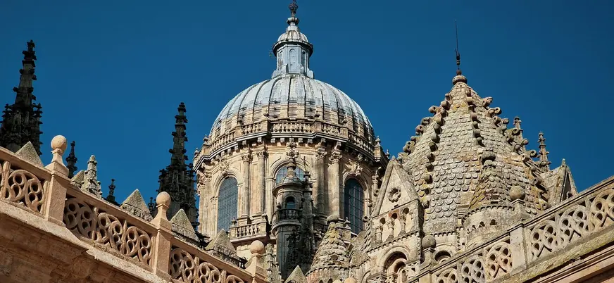 Detalle de las cúpulas y la balaustrada gótica de la Catedral Nueva de Salamanca, España, bajo un cielo azul intenso.