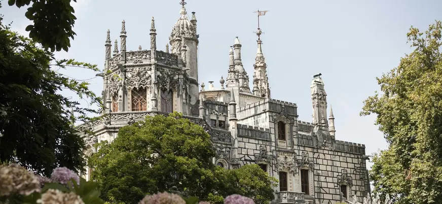 Fachada ornamentada de la Quinta da Regaleira en Sintra rodeada de árboles y flores.