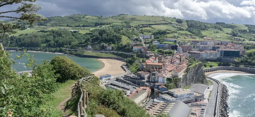 Vista aérea de Getaria con playa, puerto y colinas verdes.