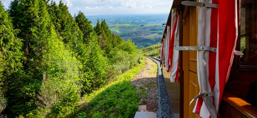 Tren de la Rhune avanzando entre bosques, con vistas al valle desde la montaña en la zona de Ainhoa.