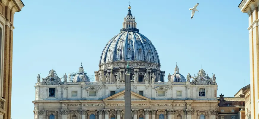 Cúpula y fachada de la Basílica de San Pedro en Ciudad del Vaticano, bajo cielo azul.
