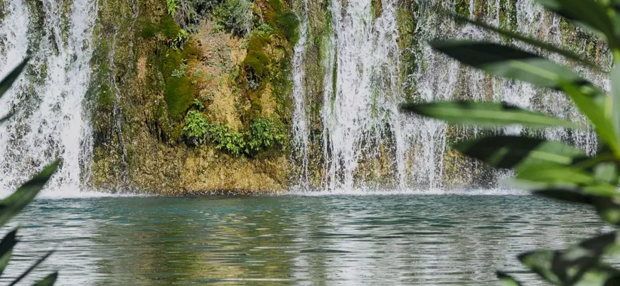 Primer plano de una cascada en las Fuentes del Algar, con agua cayendo sobre roca musgosa y vegetación.