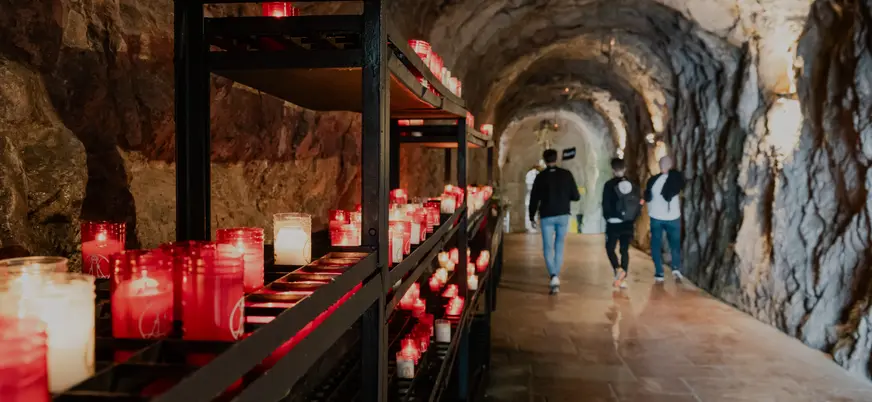Interior del Santuario de Covadonga, con velas encendidas junto a la cueva y visitantes recorriendo este lugar sagrado.