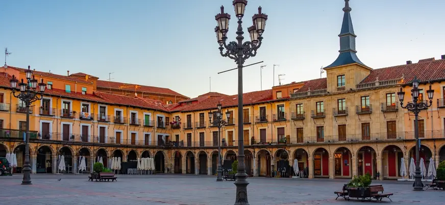 Plaza Mayor de León al atardecer, con edificios porticados, balcones y farolas de hierro, en el centro histórico.