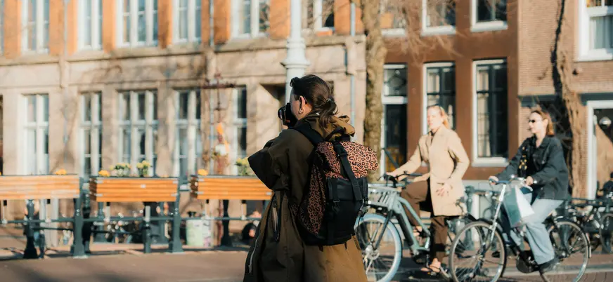 Mujer con cámara y mochila fotografiando una calle de Ámsterdam con ciclistas