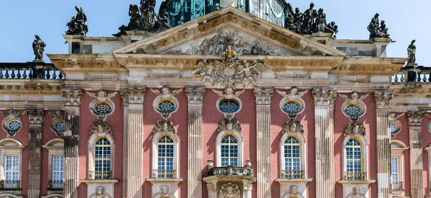 Fachada principal del Detalle de la fachada barroca del Nuevo Palacio (Neues Palais) en Potsdam, con ladrillo rojo, estatuas y cúpula.