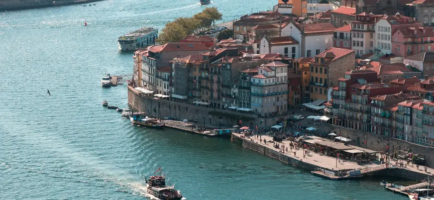 Vista de la ribera de Oporto con casas coloridas y barcos navegando por el río Duero.