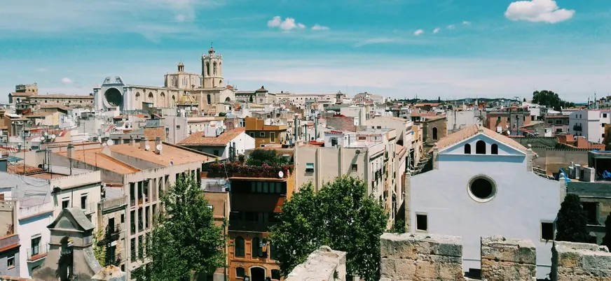 Vista panorámica de Tarragona desde lo alto, con la Catedral en el horizonte y tejados ocres bajo un cielo azul.