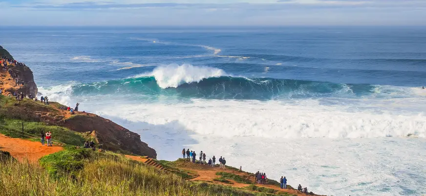 Gente observando una ola gigante rompiendo en los acantilados de Nazaré, Portugal