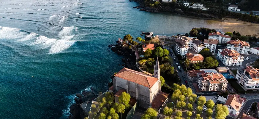 Vista aérea de la iglesia de Santa María y olas en la ría de Mundaka, Vizcaya