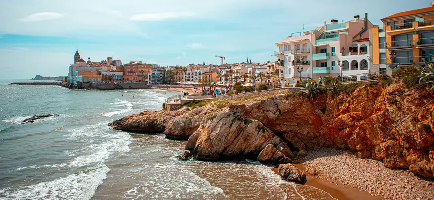 Vista costera de Sitges con casas junto al mar y acantilados bañados por las olas.