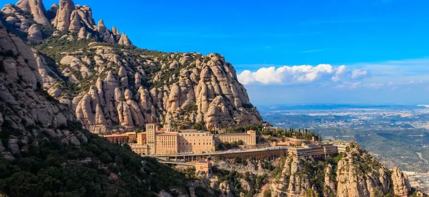 Monasterio de Montserrat rodeado de montañas rocosas bajo cielo azul.
