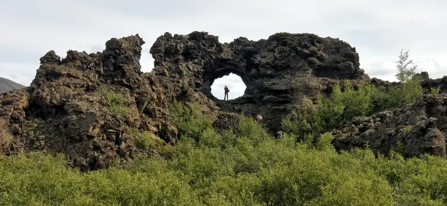 Formaciones de lava en Dimmuborgir, Islandia, con arco natural de roca volcánica rodeado de vegetación verde.