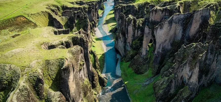 Vista aérea del cañón Fjaðrárgljúfur cerca de Kirkjubæjarklaustur, Islandia, con río azul entre acantilados verdes.