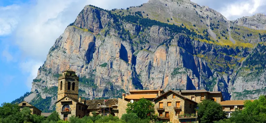 Casas de piedra con torre de iglesia bajo la Peña Montañesa en Aínsa, Huesca.