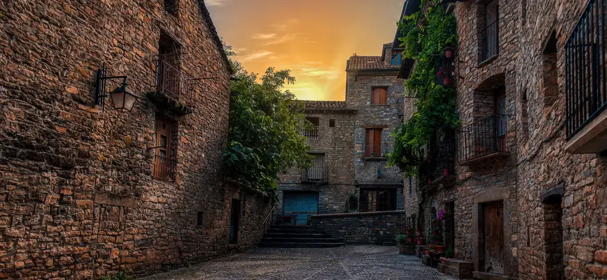 Calle empedrada rodeada de casas de piedra con balcones en la villa medieval de Aínsa.