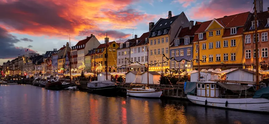 Atardecer navideño en Nyhavn, con las fachadas de colores iluminadas y el canal reflejando el ambiente mágico de Copenhague.
