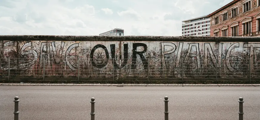 Tramo del Muro de Berlín con grafiti que dice ‘Save Our Planet’ bajo un cielo nublado