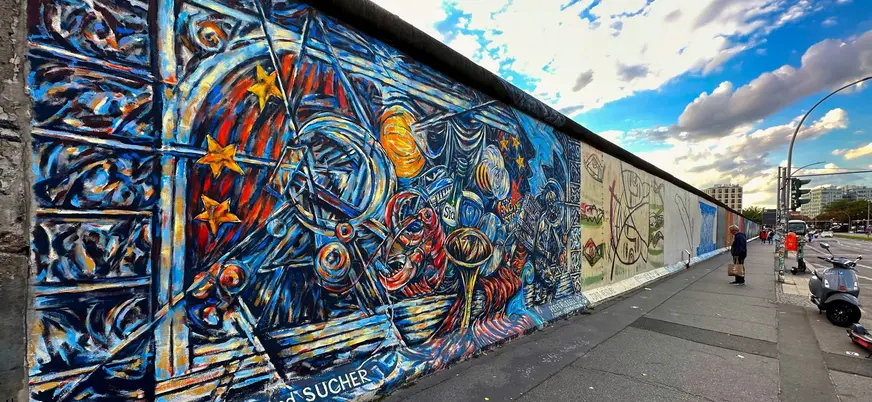 Colorido mural en el Muro de Berlín con motivos abstractos y personas observando la obra