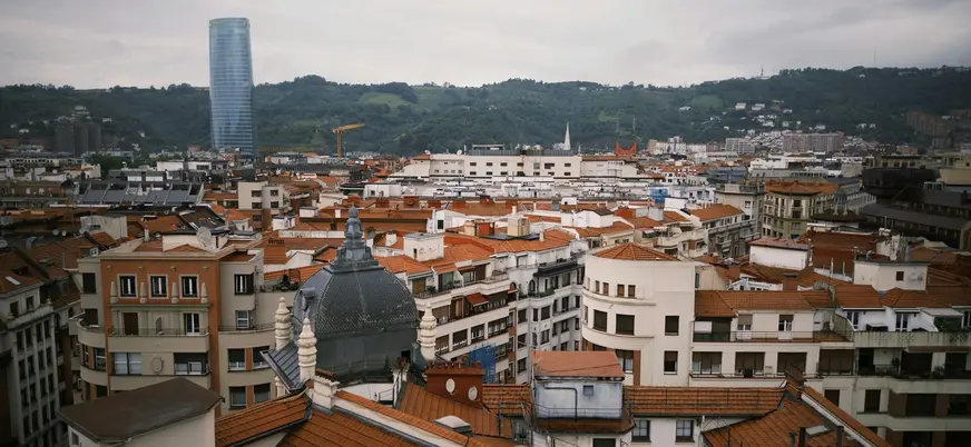 Tejados del centro de Bilbao con la torre Iberdrola y montes verdes al fondo.