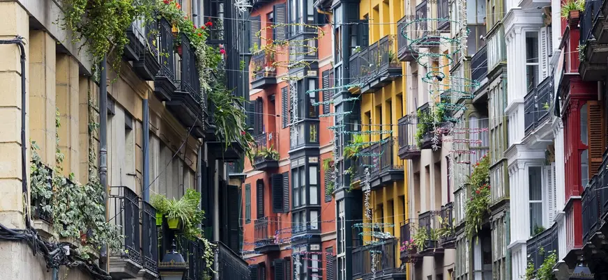 Fachadas coloridas y balcones con plantas en una calle estrecha del Casco Viejo de Bilbao.