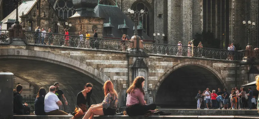 Jóvenes sentados junto al canal bajo el Puente de San Miguel en Gante.