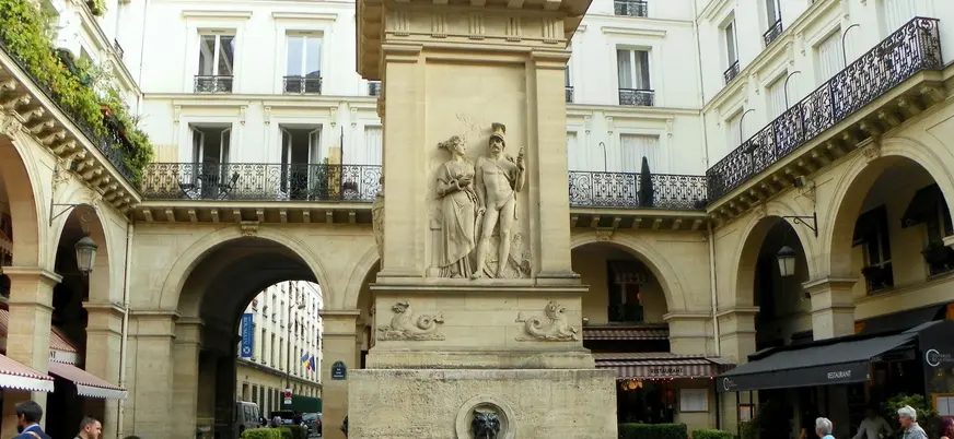 Fuente de Jussieu en una plaza rodeada de edificios clásicos y terrazas en París