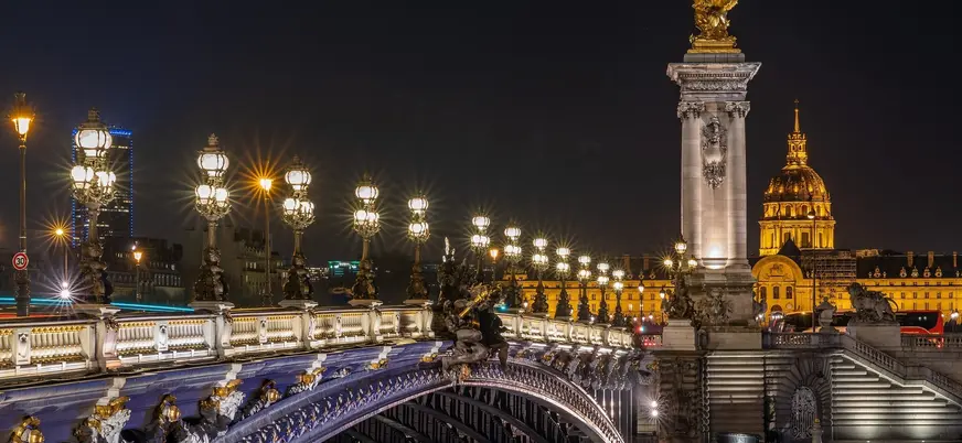 Puente Alejandro III iluminado de noche con Los Inválidos al fondo en París.