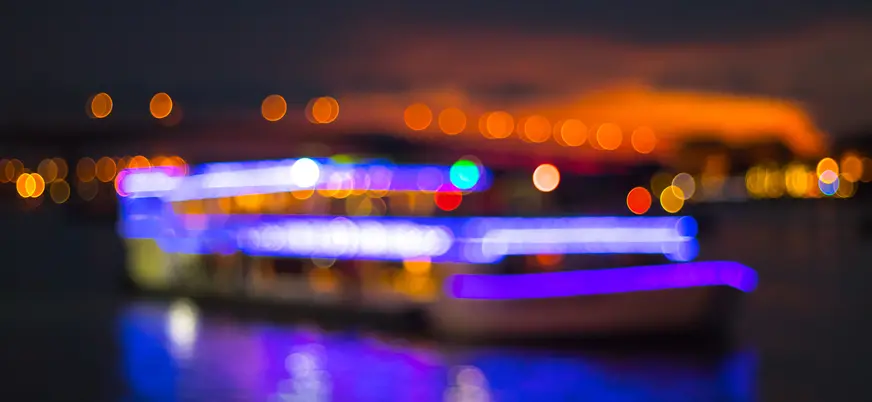 Barco iluminado con luces de colores navegando de noche.