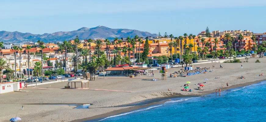 Playa de Salobreña con sombrillas, palmeras y edificios bajo montañas soleadas
